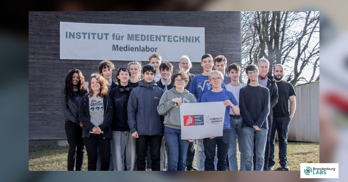 EIN-Activity-2026_1200-x-628px A group of students is standing with Prof. Karlheinz Brandenburg in front of the Institute of Media Technology at the Technical University of Ilmenau. Some of the students are holding a banner from the European Inventor Network.
